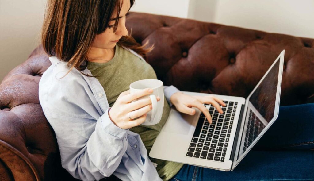 Chica consulta ordenador mientras sujeta una taza en la mano