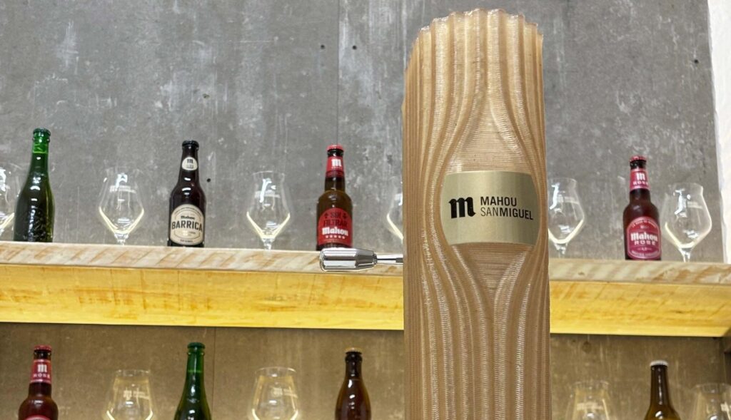 Grifo de cerveza Mahou en una barra con otros botellines en una pared e fondo