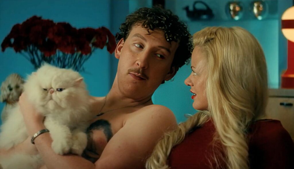 Hombre sin camiseta sujetando un gato con una mujer a su lado. Ambos sentados en un sofá.