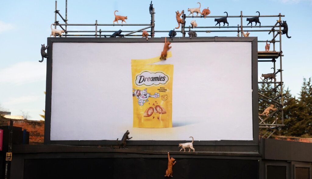 Valla publicitaria de Dreamies con maquetas de gatos escalándola