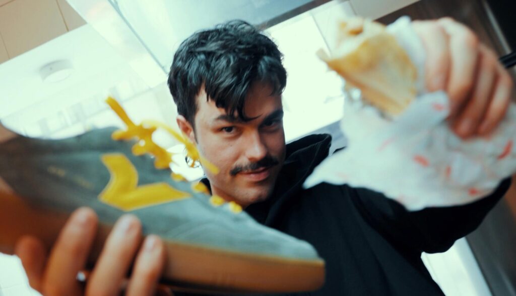 El tiktoker Peldanyos mirando a cámara mientras sujeta con una mano una zapatilla Victoria y con otra un shawarma