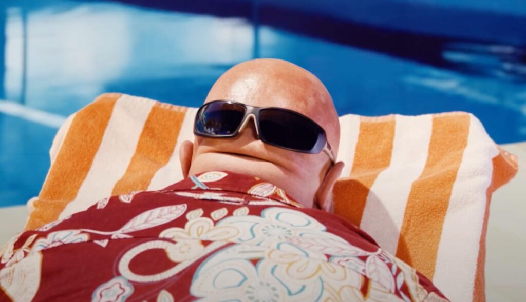 Persona calva tomando el sol en una piscina boca abajo, con unas gafas de sol sobre la nuca