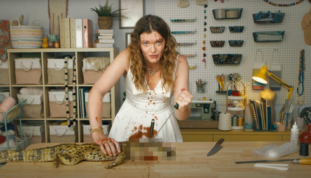 Mujer jóven clavando un cuchillo en la cabeza de un cocodrilo para enseñar a hacer un bolso birkin en la nueva campaña de PETA