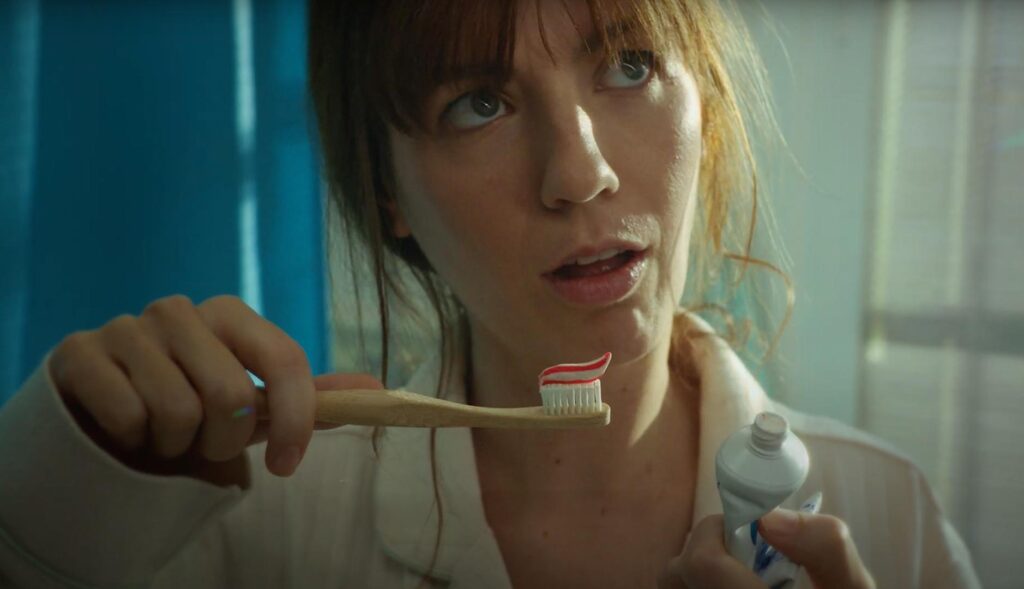 Mujer joven con un cepillo de dientes en la mano, dentro de un baño.