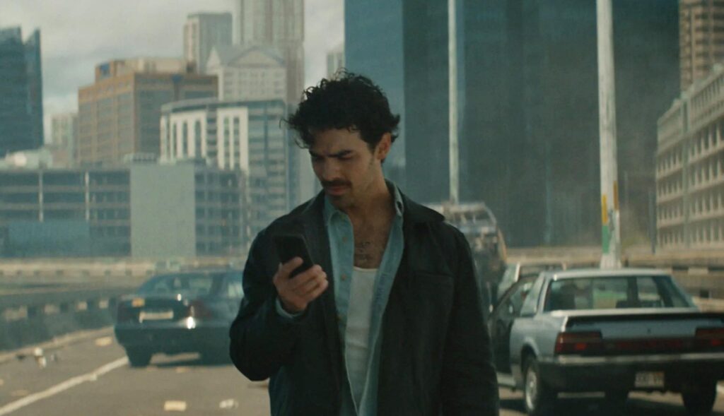 Joe Jonas mirando un teléfono móvil en una ciudad arrasada y sin habitantes