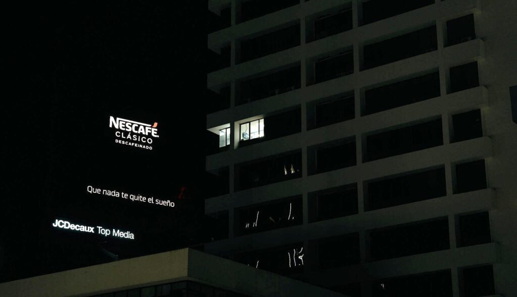 Valla publicitaria de Nescafé por la noche frente a un edificio de viviendas
