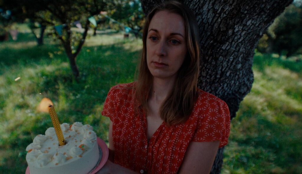 una mujer con cara triste sujeta una tarta de cumpleaños con una bengala encendida