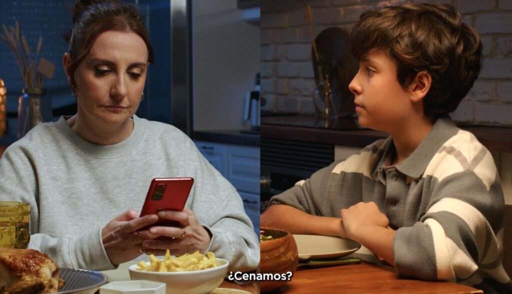 una madre usa el movil en la mesa mientras su hijo espera mirándola para empezar a cenar