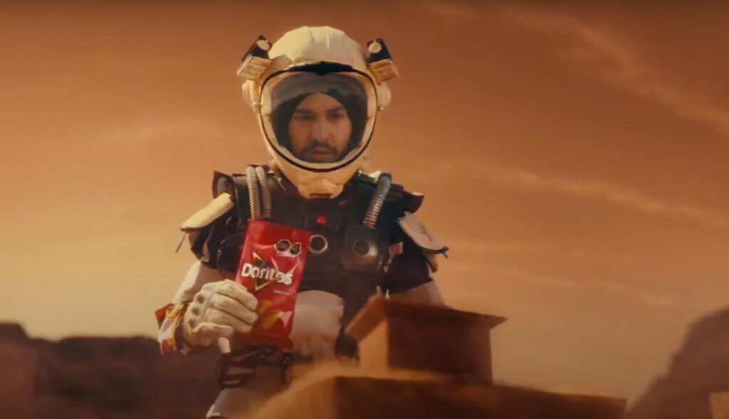 Persona disfrazada de astronauta con una bolsa de Doritos en la mano