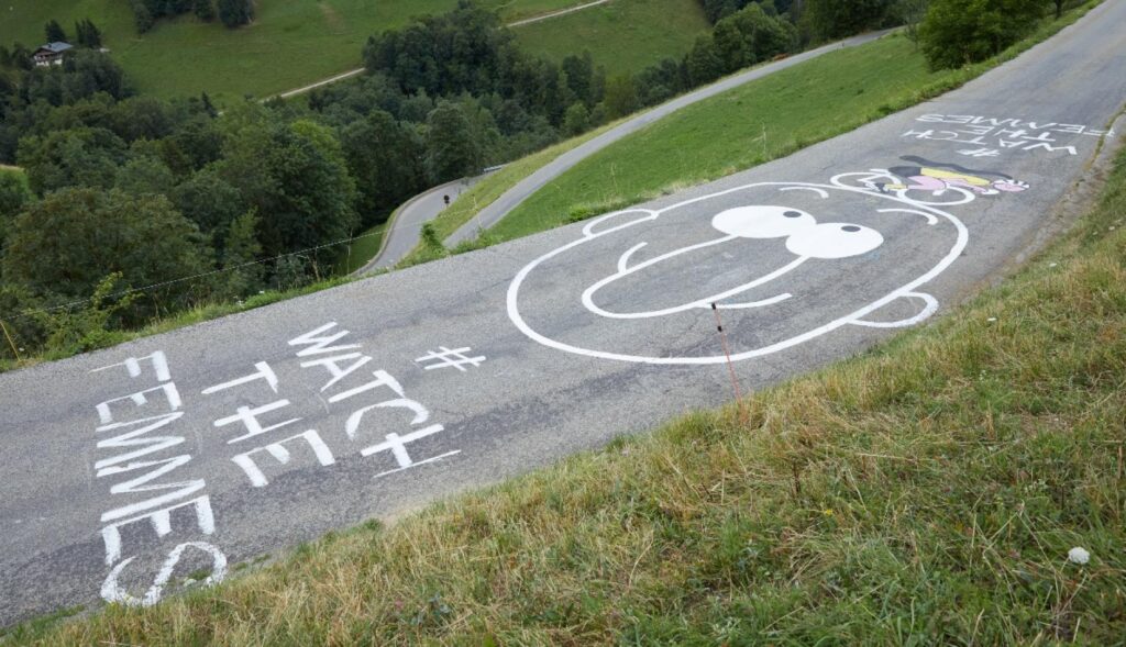 un grafiti en la carretera que dice watch the femmes junto al dibujo de una cara con nariz con forma de pene