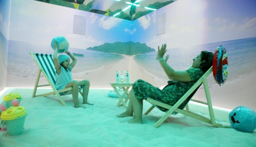 una madre y su hija juegan a la pelota en la sala inmersiva con arena y tumbonas