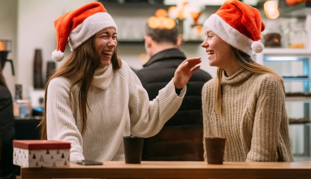 dos chicas tomando café y riendo con gorros de papá noel