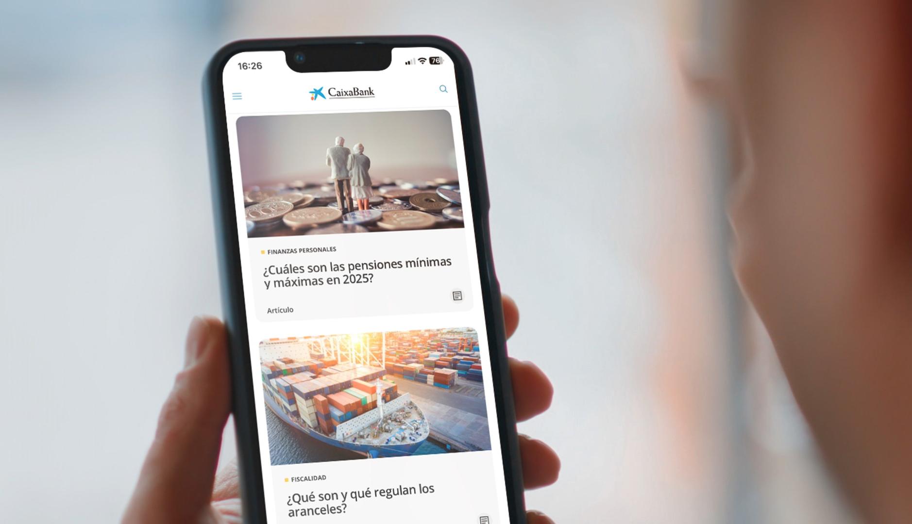 Una persona sujeta un móvil con artículos de CaixaBank