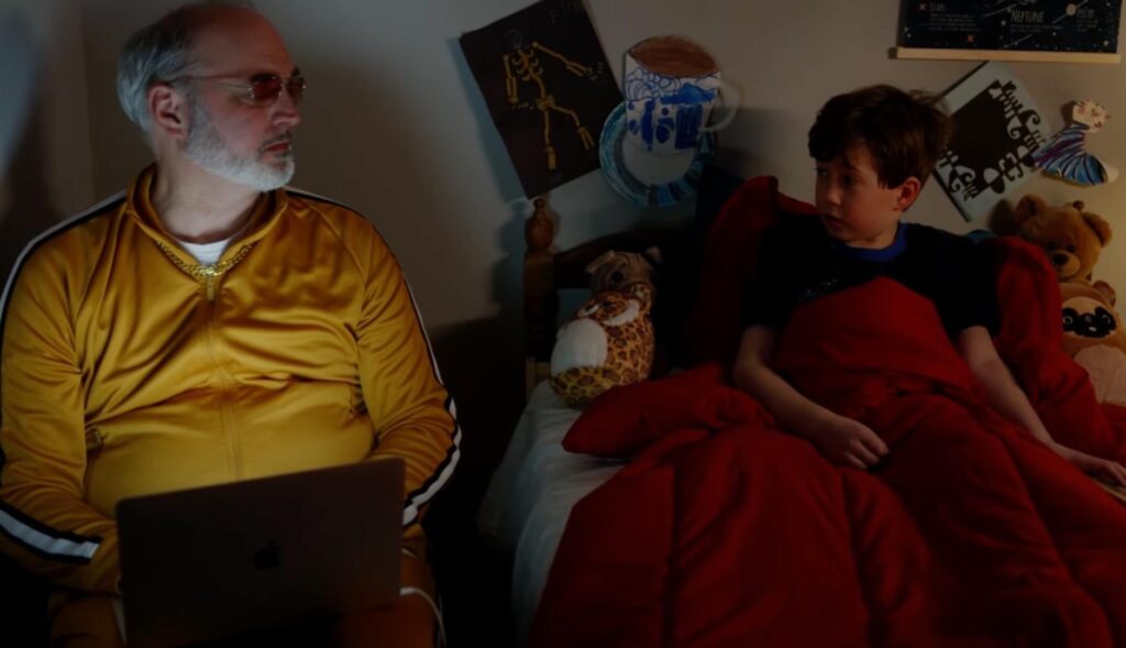 Un niño en su cama mirando a un señor que tiene al lado con un ordenador