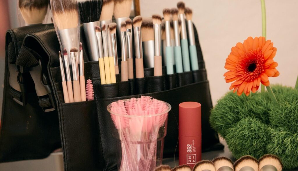 Un set de brochas de maquillaje junto a una flor naranja