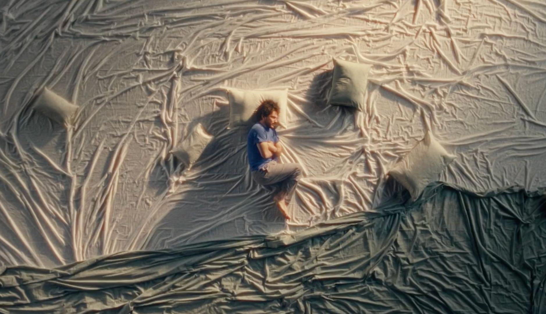 Plano cenital de un hombre acurrucado sobre telas y almohadas