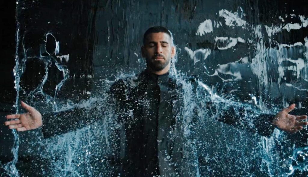 Ilia Topuria con los brazos en cruz bajo una cortina de agua vestido