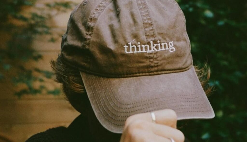 un hombre sosteniendo una gorra marrón en la cabeza donde se puede leer "thinking"