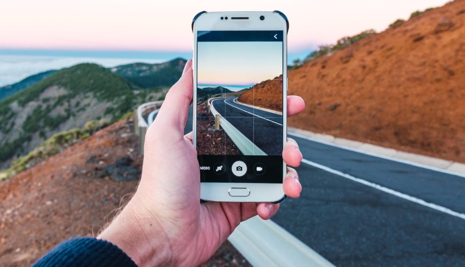 Una mano sosteniendo un móvil para hacer una foto del paisaje de una carretera de montaña