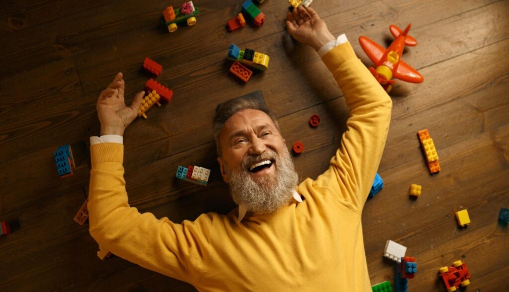 Un hombre mayor tumbado en el suelo rodeado de piezas de Lego