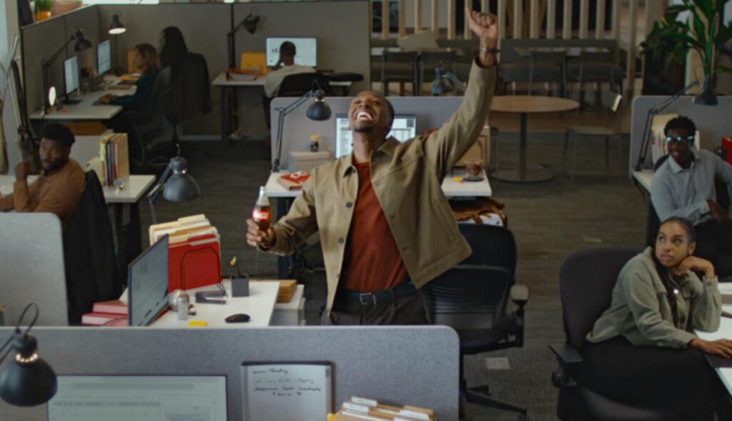 Un hombre en una oficina celebra un gol con una coca-cola en la mano