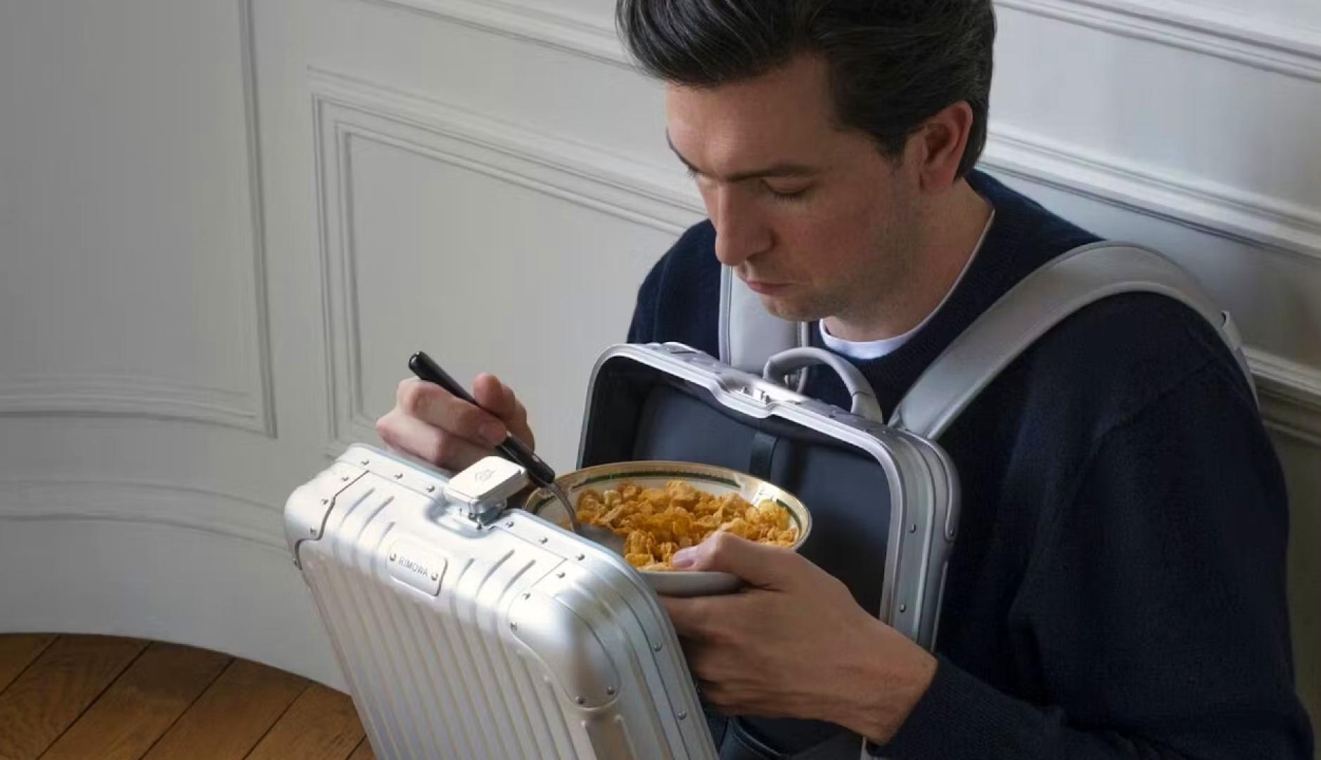 Nicholas Braun sentado en el suelo comiendo cereales dentro de la mochila de Rimowa