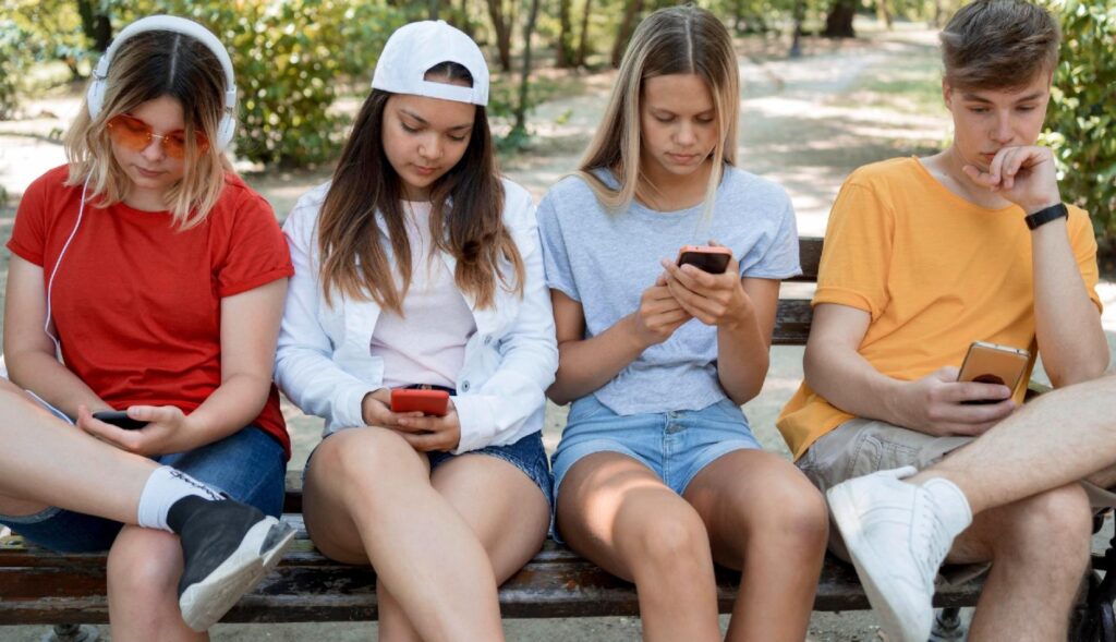 Cuatro jóvenes sentados en un banco, mirando el teléfono sin hablar entre ellos