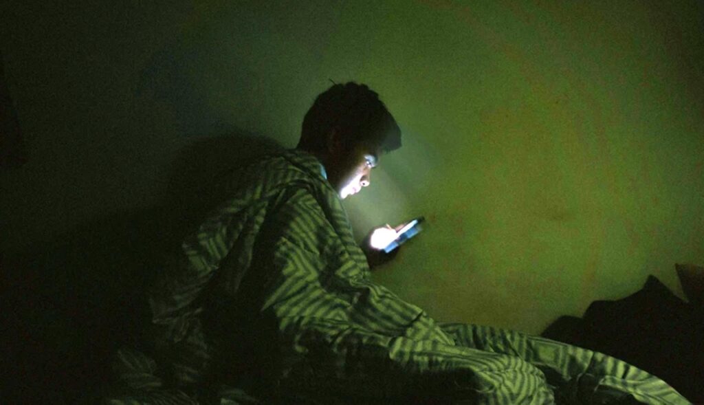 Un niño mirando el móvil en la cama a oscuras