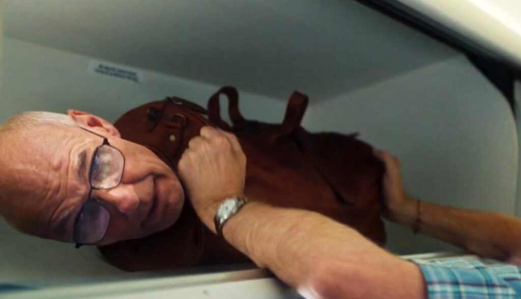 Una maleta con cabeza de señor que se está colocando en el maletero del avión