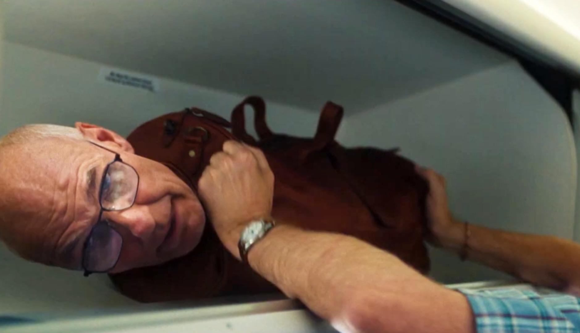 Una maleta con cabeza de señor que se está colocando en el maletero del avión