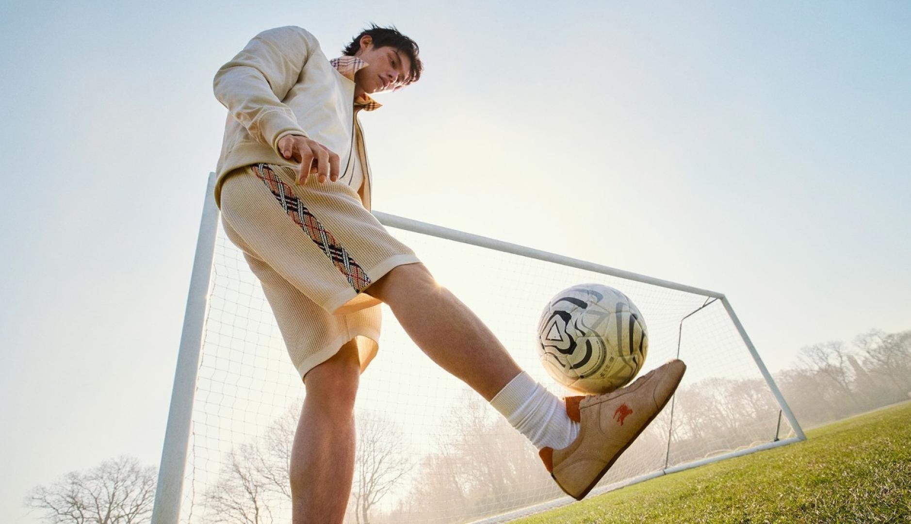 Un chico vestido de Burberry junto a una portería de fútbol dando un toque al balón