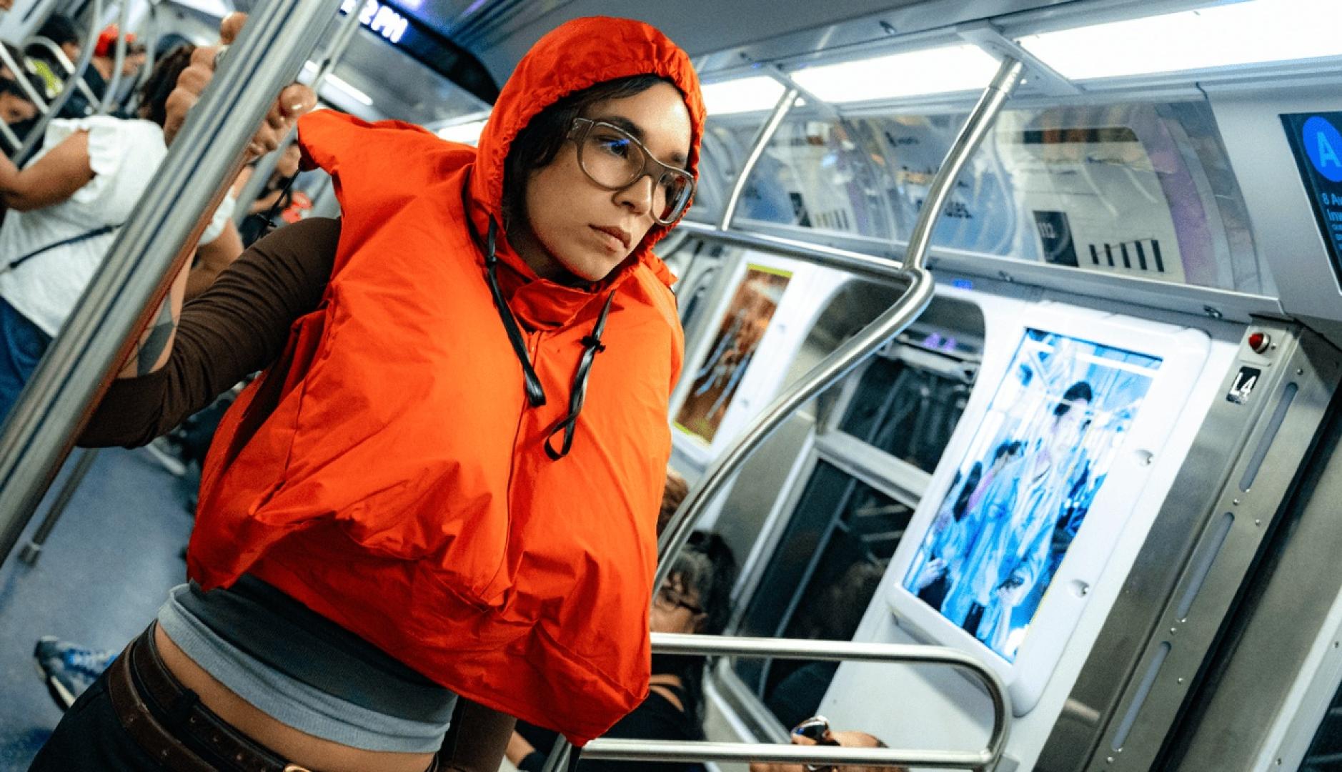 Una chica en un vagón de metro con el chaleco naranja puesto