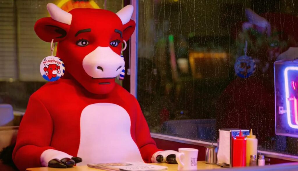 La vaca sentada en un bar con una cristalera lluviosa y el rostro triste