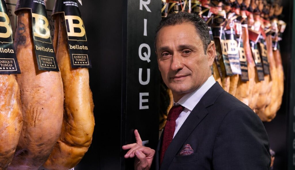 Enrique Tomás junto a unos jamones colgados en la tienda