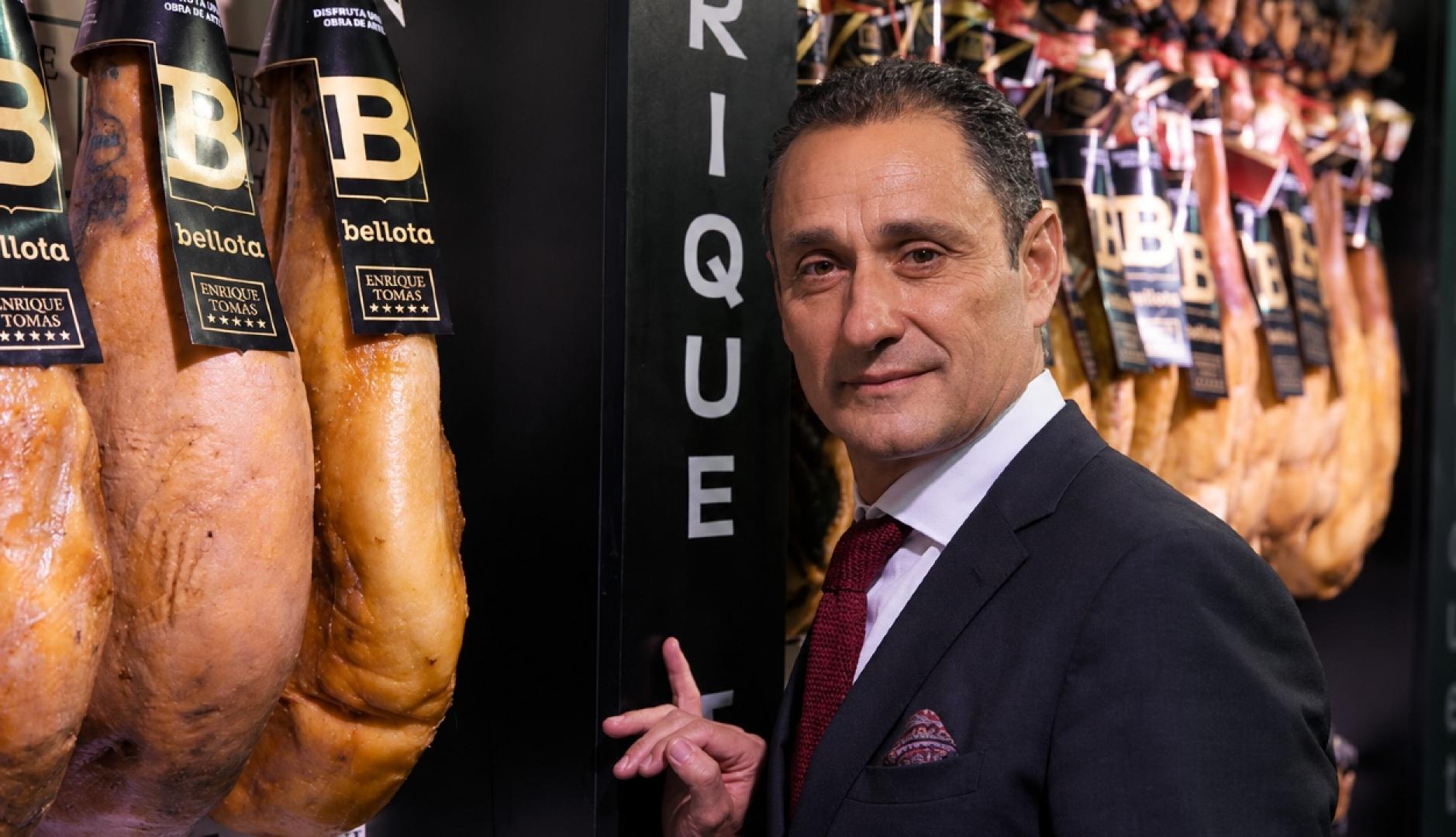 Enrique Tomás junto a unos jamones colgados en la tienda
