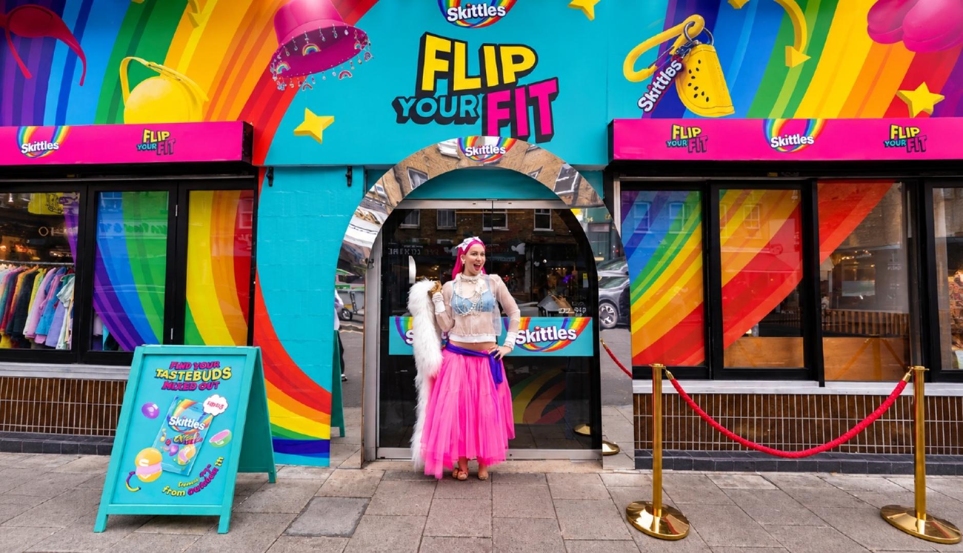 Una chica vestida de colores frente a la pop-up de Skittles