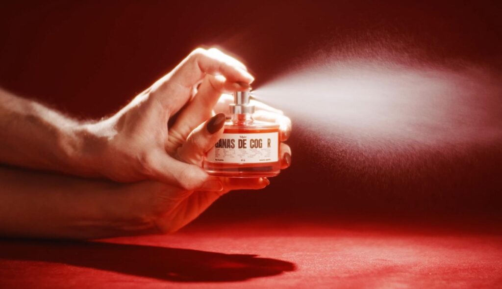Las manos de un hombre y una mujer sosteniendo el bote del que sale perfume
