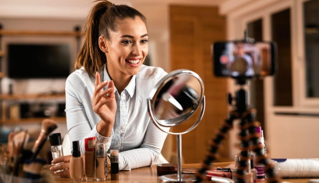 Una chica con productos de belleza grabándose con el teléfono y un espejo