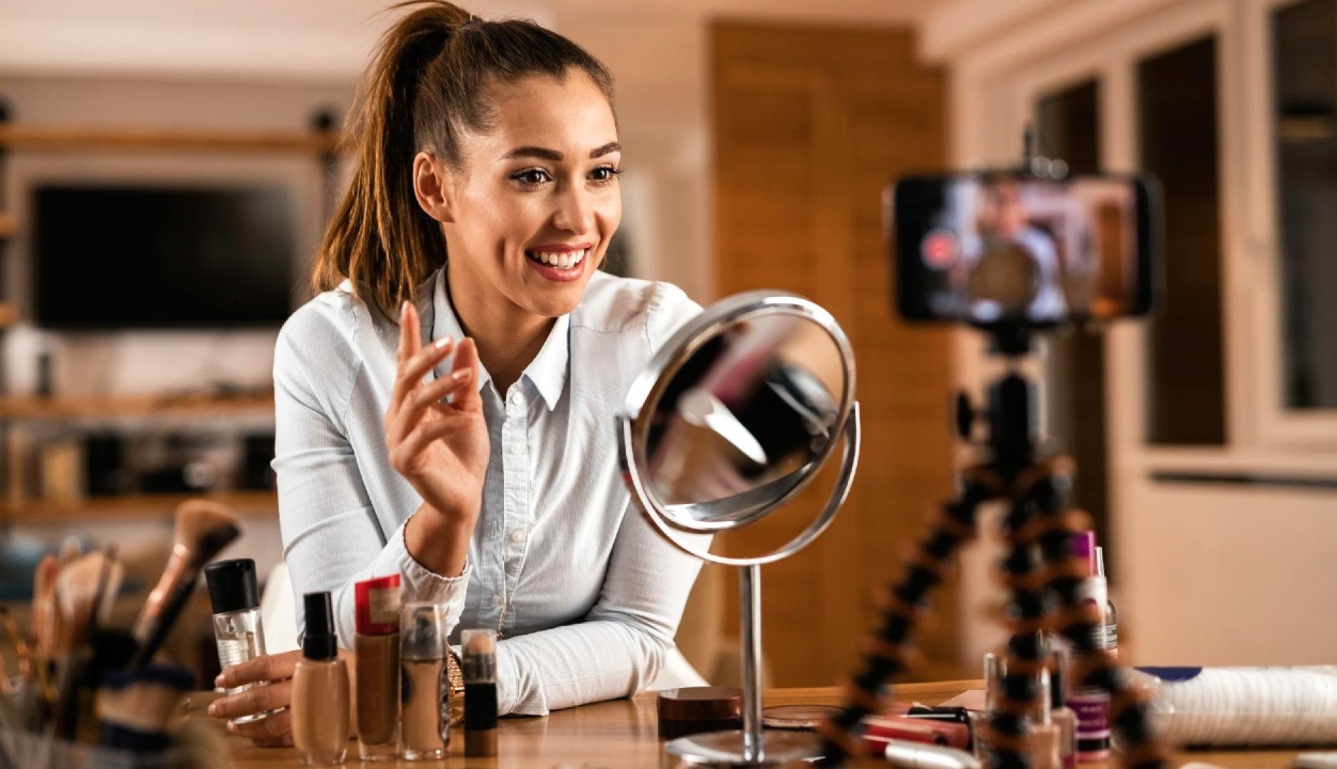 Una chica con productos de belleza grabándose con el teléfono y un espejo